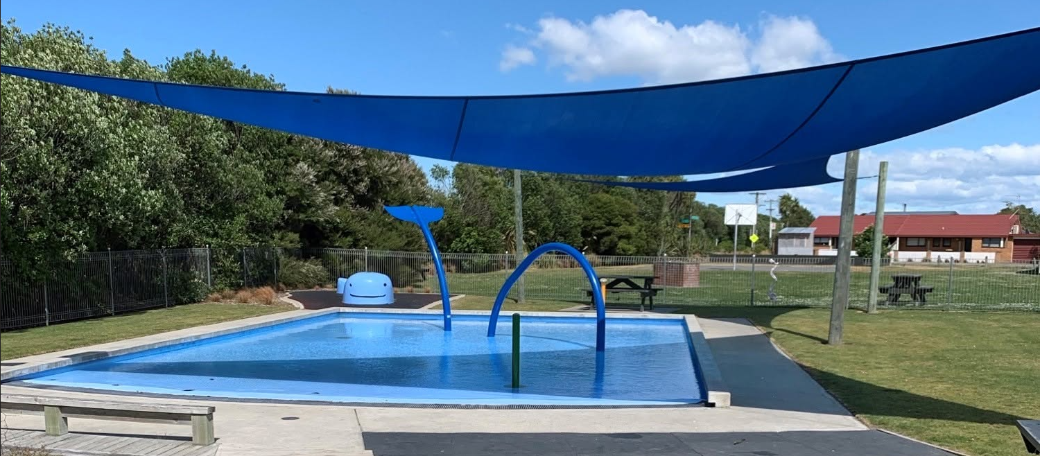 Waikuku Beach paddling pool beneath blue shade sails, with its water-play features